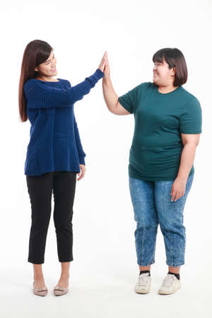 Two fat and skinny Asian women standing on a white background The two of them touched each other with their hands. Happy smile. healthy weight loss concept.の写真素材
