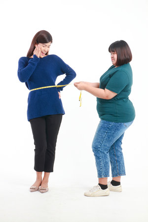 Fat Asian woman holding a tape measure around her waist to measure waist circumference of skinny women Check her waist size to help plan for weight gain or weight loss. Concept of health care. Dress.の写真素材