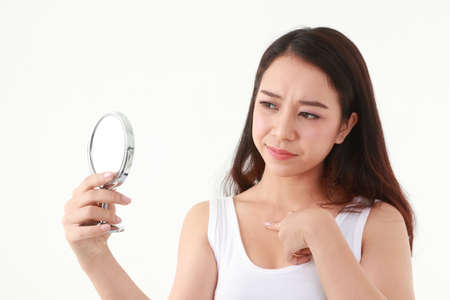Beautiful Asian woman with long hair Hold a mirror and look at the pimples on her chest. Beauty concept. Beautiful skin care. Acne treatment. White background.の写真素材