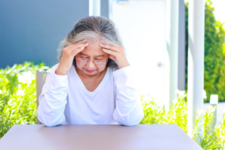 Asian elderly woman sitting in the garden outside the house She has a headache. Health care concepts, brain diseases of the elderly. Retirement health insuranceの写真素材