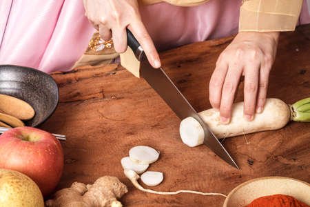 Girl wearing hanbok, making chopped kimchi, radish and carrots to mix with Chinese cabbage. Korean food concept from folk wisdomの写真素材