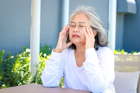 Asian elderly woman sitting in the garden outside the house She has a headache. Health care concepts, brain diseases of the elderly. Retirement health insuranceの写真素材