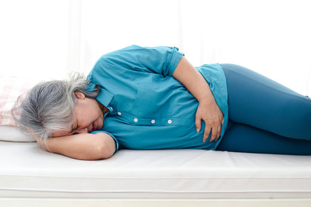 Asian elderly woman has a stomachache. She lay on the white bed. Elderly health concept. Health insurance and elderly careの写真素材