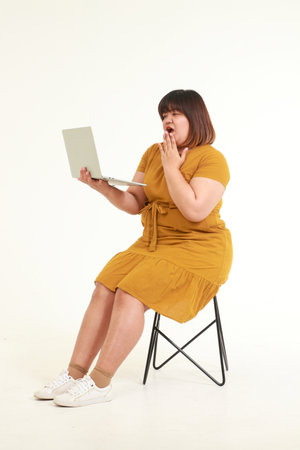 Asian fat woman sitting on a chair on a white background She holds a laptop to work. Concept of working online. fashion dressの写真素材