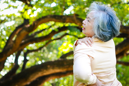 elderly woman walking in the park She had severe shoulder pain, inflamed ligaments, partial torn ligaments. The concept of shoulder pain in the elderly. health care. copy spaceの写真素材