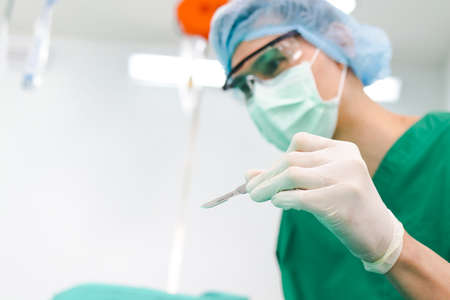 Asian professional surgeon holding a scalpel with glasses and wear gloves and a mask In the operating room in the hospital. Concept of medical services. cosmetic surgery. Copy spaceの写真素材