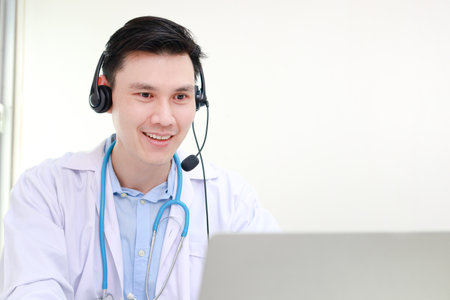 Asian male doctor smiling beautifully Providing treatment services for patients with online conversations via the Internet on laptop computers. online doctor concept. Copy spaceの写真素材