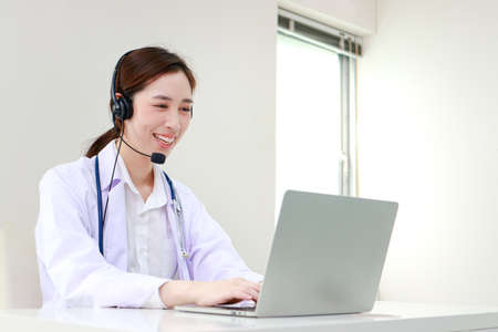 Asian female doctor smiling beautifully Providing treatment services for patients with online conversations via the Internet on laptop computers. online doctor concept. Copy spaceの写真素材