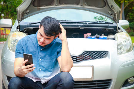 asian men Holding a black smartphone, call your insurance company or technician for help. because he was in an accident or the car engine broke down. car insurance conceptの写真素材