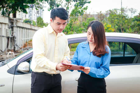 Woman signing paperwork to claim car insurance with insurance company employee Because she was...