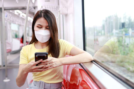 Concept of traffic and transportation. Asian female passenger wearing a mask holding a smartphone chatting online via the Internet.の写真素材