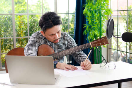 Asian musician artist Sit and compose music in the glass room at home. online music learning conceptの写真素材