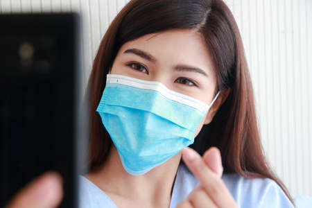 Asian female patient wearing mask in hospital patient room She holds a smartphone online talking to her family. Concept of medical services.の写真素材