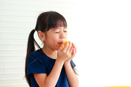 Nutrition for school-age children. Cute little Asian girl enjoys eating oranges. Choosing the right food according to the age of the child for good healthの写真素材