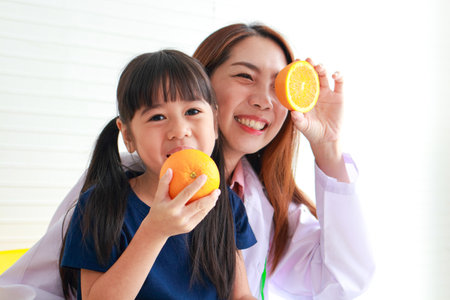 Nutrition for school-age children. A beautiful nutritionist or doctor with a little girl holding an orange. Choosing the right food according to the age of the child for good healthの写真素材