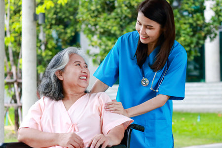 Asian female doctor wearing surgical gown Touching the arm of an elderly patient sitting on a wheelchair encouraging, do not worry about treatment. Concept of medical services in hospitals.の写真素材