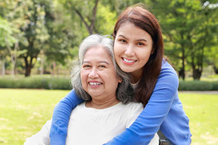 Elderly mother and daughter smiling happily in the park in the morning. Family concept. Health care for the elderly in retirement age. Nurses take care of the elderly. Close-up photo.の写真素材