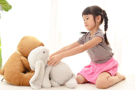 cute little asian girl having fun She sits with a teddy bear and a big rabbit on the white bed. concept of family, friendshipの写真素材