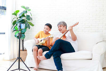Asian father and son playing music together at home They are happy with the music. Learn music online through your smartphone. leisure activities. modern communication new lifestyleの写真素材