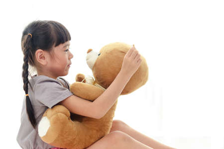 cute little asian girl having fun She hugged a big brown teddy bear on the white bed. concept of family, friendshipの写真素材