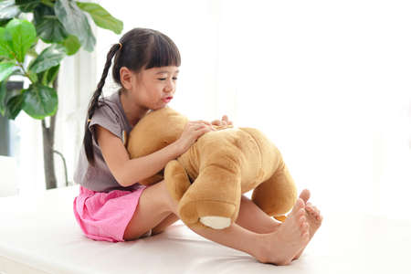 cute little asian girl having fun She hugged a big brown teddy bear on the white bed. concept of family, friendshipの写真素材