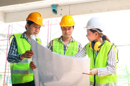 Architects and Engineers and Builders Holding a blueprint discussing building construction plans at...