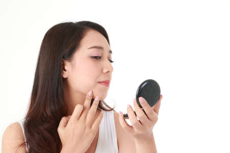 Beautiful Asian woman holding a mirror looking at the pimples on her right cheek. She was very stressed. Beauty concept, beautification, beauty skin care. white background.の写真素材