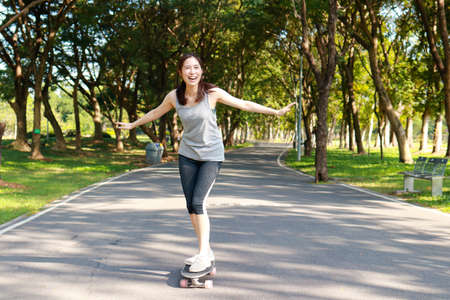 Asian woman exercising in the morning Practice basic skateboarding on the streets of the park. Playing sports for health makes you strong and happy.の写真素材