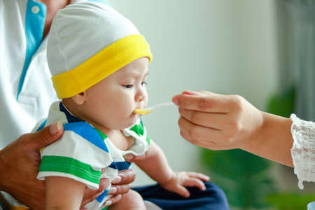 A mother feeds an adorable Asian baby boy. family concept Caring for newborn babies. Baby Food...