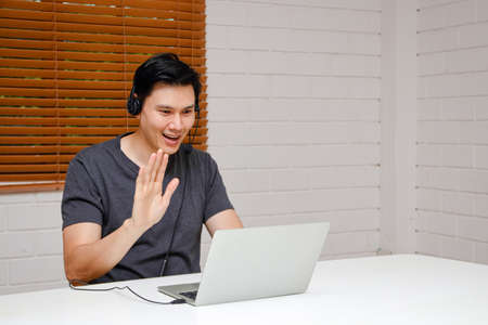 Asian men working from home He wears headphones and works online on his laptop computer. Smiling, happy, online meeting, greeting colleagues. Business concept. Small entrepreneurs. freelanceの写真素材