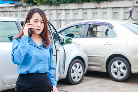 Auto insurance concept. A woman working in an office driving a car has an accident. holding a smartphone to inform the insurance officer to take careの写真素材