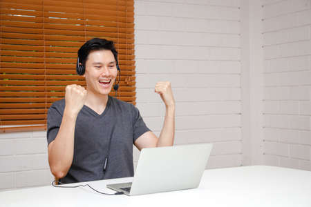 Asian men working from home He wears headphones and works online on his laptop computer. Smiling glad that the job was successful. Business concept. Small entrepreneurs. freelanceの写真素材