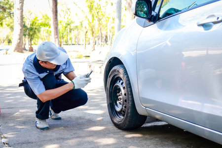 auto repair technician Holding a smartphone to take pictures of the wheels of a car that has an accident with a broken tire on the road. Transportation concept. service businessの写真素材