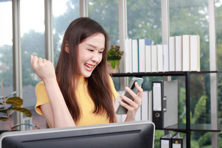 Young Asian businesswoman holding a smartphone smiling happy at work. Work on finance and marketing projects. Entrepreneurial concept. use of technology in communicationの写真素材