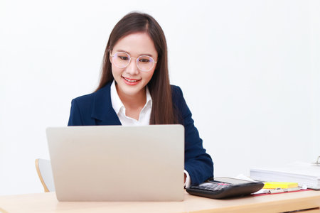 female manager wearing a blue suit sitting at the desk She is wearing glasses typing data on her laptop computer. Concept of businesswoman, entrepreneurs. copy space. white backgroundの写真素材