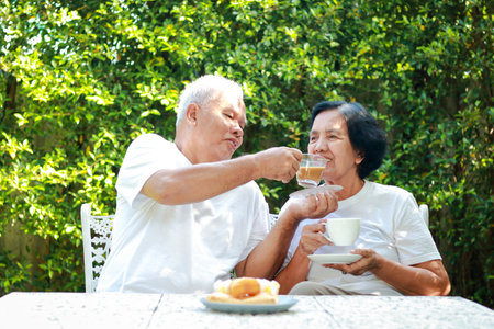 Happy Asian elderly couple Sit and drink coffee together in the morning in the garden of the house. The concept of family taking care of each other. life in retirementの写真素材
