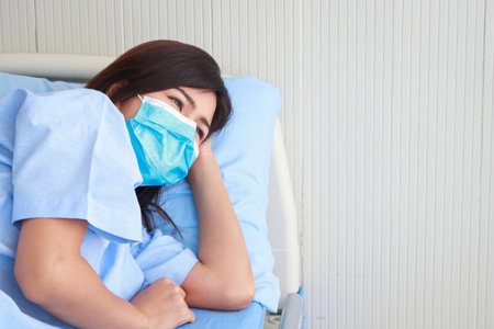 Asian female patient stressed and worried wear a mask Lie on the bed in the patient room. The concept of health insurance. Hospital medical servicesの写真素材