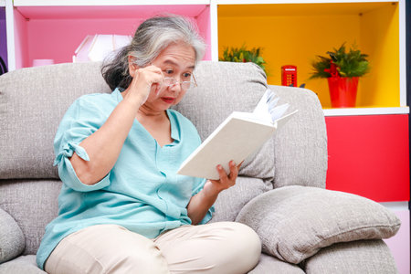 Asian elderly woman Sitting on the sofa in the house reading a book. The concept of life of the elderly in retirement age. health careの写真素材