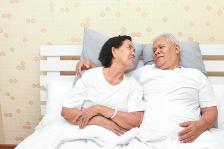 Asian elderly couple lying in bed in the bedroom Happy smile. family concept health care, health insurance for seniorsの写真素材