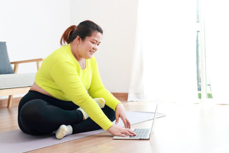 Fat Asian women exercise to lose weight. sitting on the floor watch online video on laptop Exercise according to a fitness trainer. sports concept healthy exercise. copy spaceの写真素材