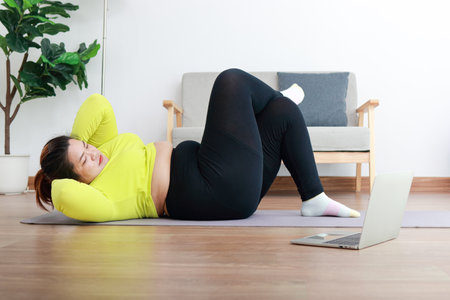 Fat Asian women exercise to lose weight. lying on the wooden floor in the house Perform exercises by following online video fitness trainers on your laptop computer. sports concept healthy exerciseの写真素材