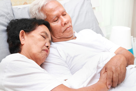 An elderly Asian couple sleeps cuddling in bed in the bedroom. family concept health care, health insurance for seniorsの写真素材