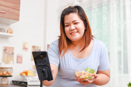 Fat Asian woman cooks organic food in her kitchen at home. Record online video via smartphone Make content published on social media. Influencer concept. healthy cooking for weight lossの写真素材