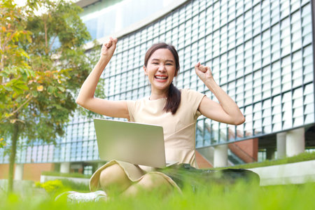 Portrait of a beautiful Asian university student. she smiles happy Sit on the grass and use a laptop computer to learn on campus. education conceptの写真素材