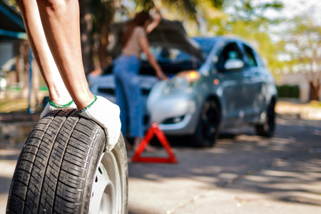 Auto mechanic changing car wheels To a woman who had a car accident with a tire leak and was parked on the side of the road. Car insurance concept.の写真素材
