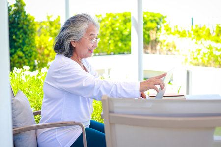 Asian elderly woman relaxing at home playing laptop computer online chatting with friends. The concept of living in retirement to be happyの写真素材