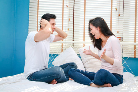 stressed couple sitting on the bed quarreling The man covered his ears with his hands. concept of family problemsの写真素材