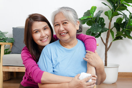 Portrait of a daughter with an elderly Asian mother smiling happily. Sit and cuddle in the living room of the house. Family concept. Health care.の写真素材