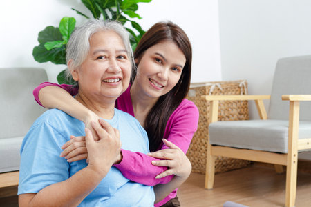 Portrait of a daughter with an elderly Asian mother smiling happily. Sit and cuddle in the living room of the house. Family concept. Health care.の写真素材