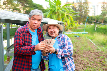 Asian elderly couple farming agriculture smiling happy holding Thai baht as income from agriculture. Solar system. concept of using modern agricultural technology. copy spaceの写真素材